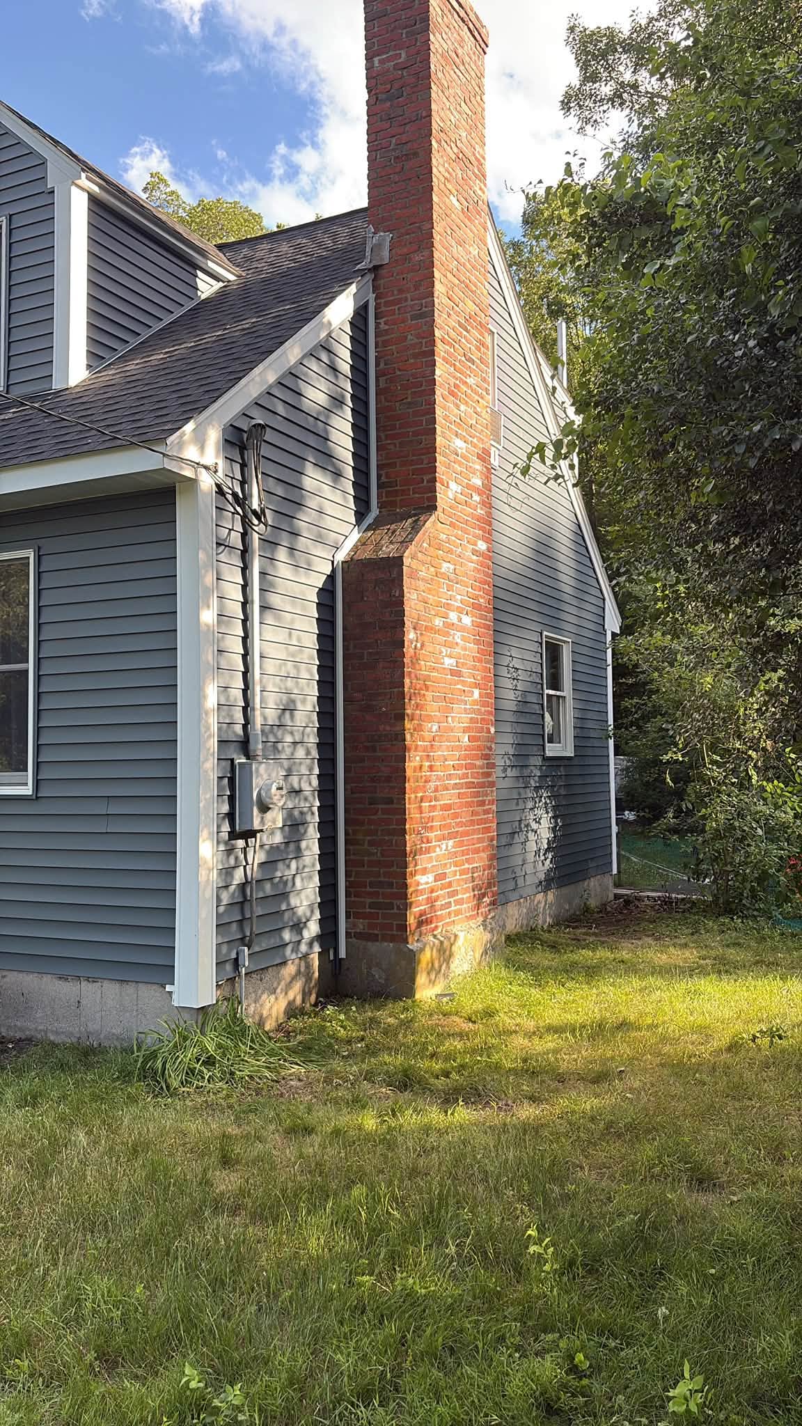 Back corner of a blue-gray Cape with its brick chimney