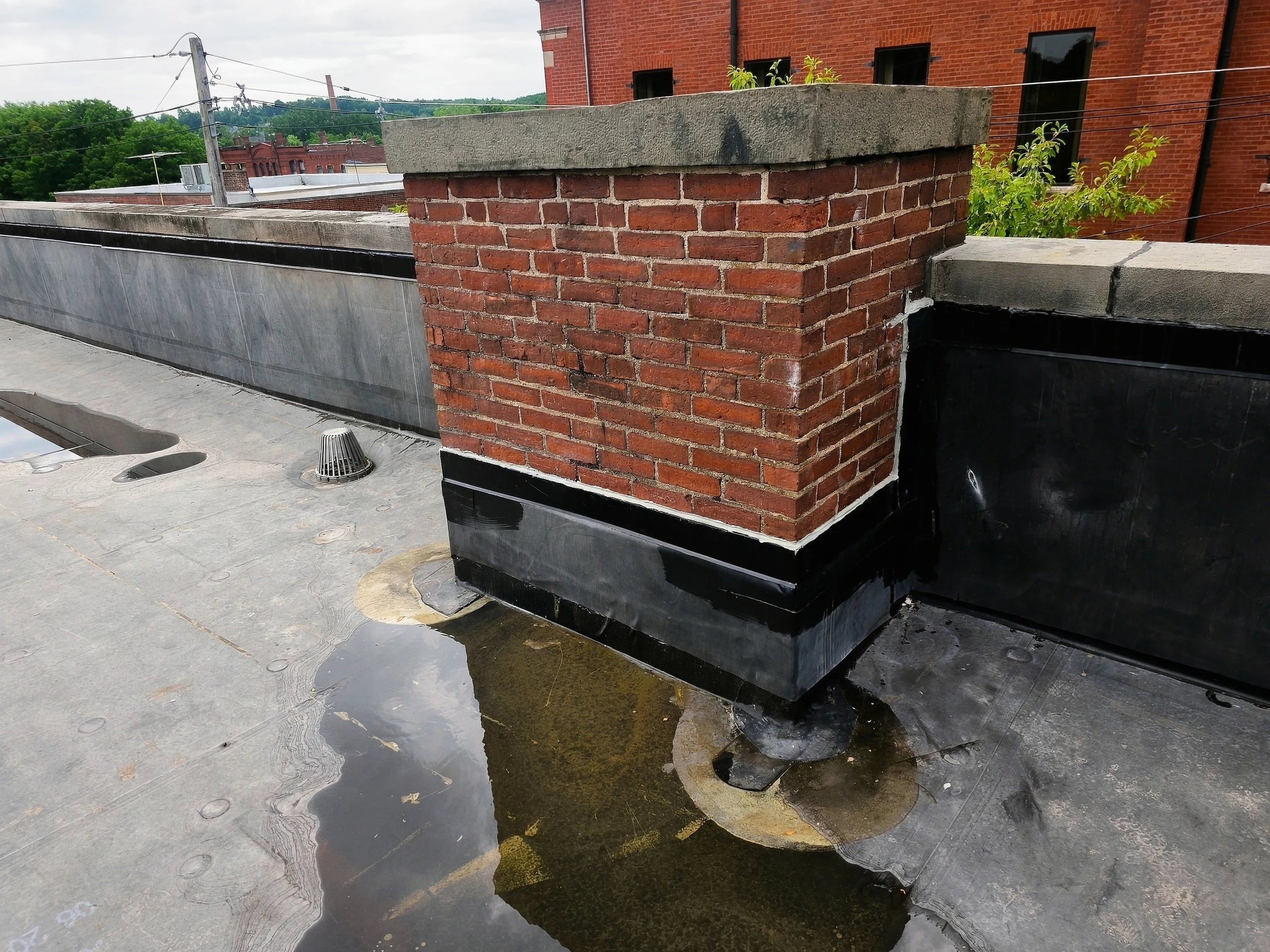 Flat-roof membrane and perimeter details around a brick chimney.