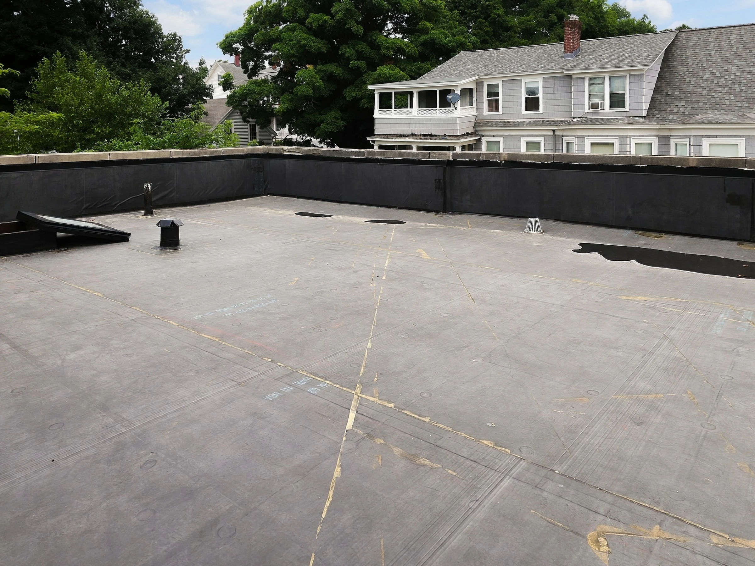 Wide view of flat-roof membrane and roof penetrations beside a parapet wall.