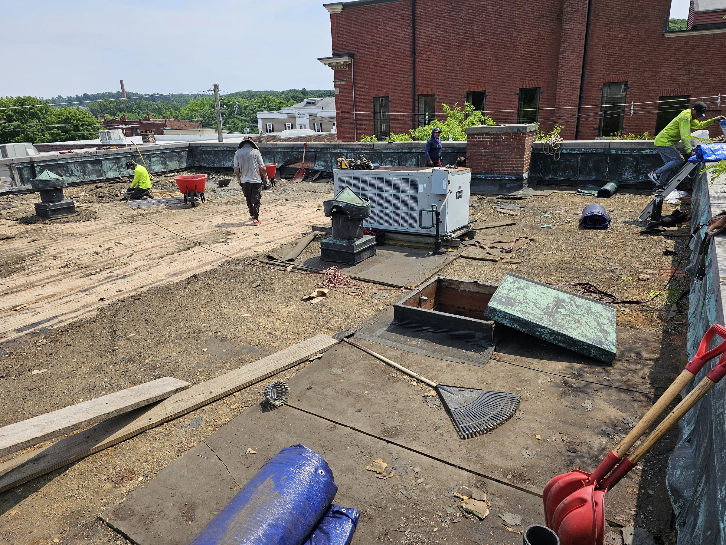 Roofing crew on a flat roof during tear-off, with exposed deck and equipment.